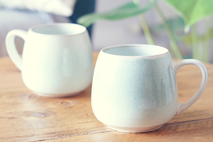 two teacups on wooden table with plant in background